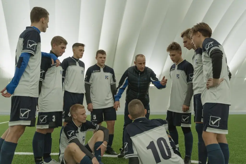 A coach passionately instructs his soccer team during a practice session inside a sports dome.