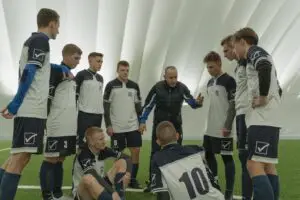 A coach passionately instructs his soccer team during a practice session inside a sports dome.